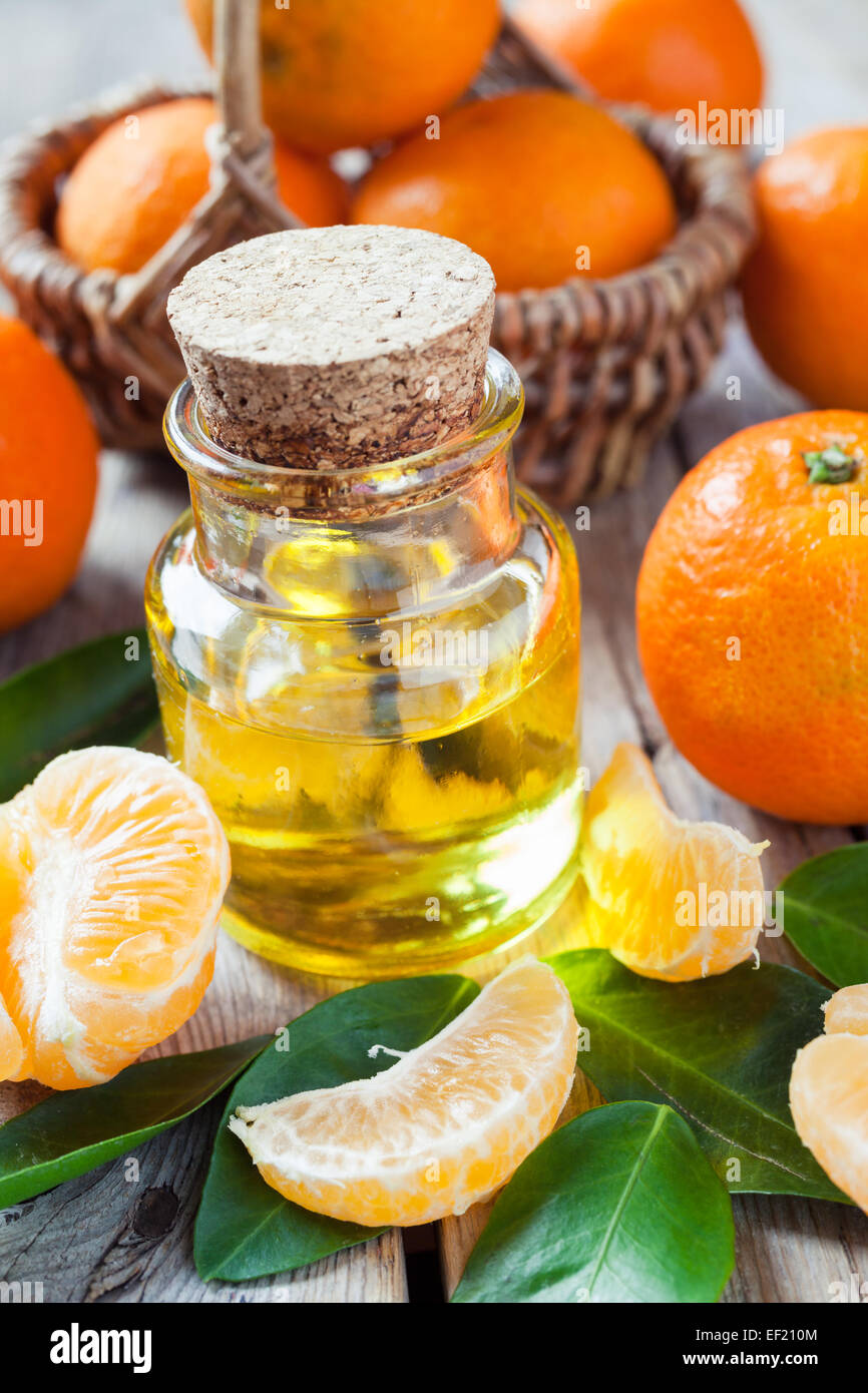 Bottle of essential citrus oil and ripe tangerines in basket on old wooden kitchen table. Stock Photo