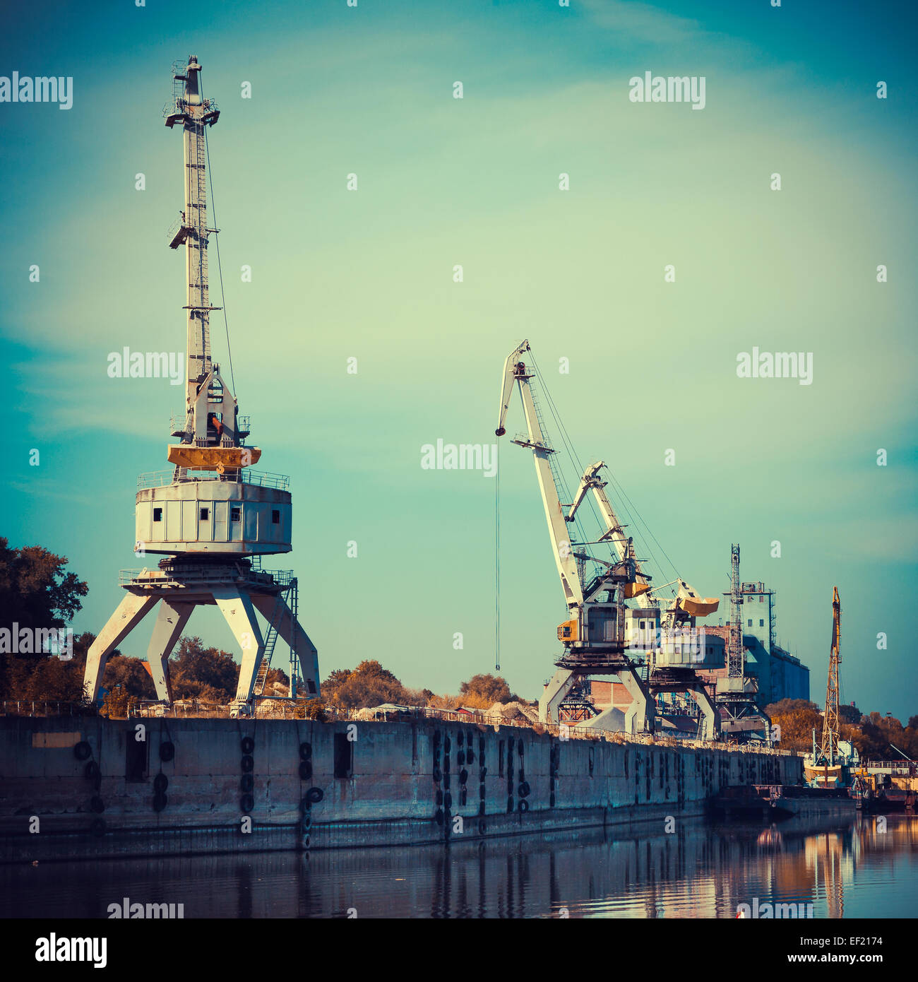 Working cranes for cargo at the shipyard docks in river port, vintage stylized. Stock Photo