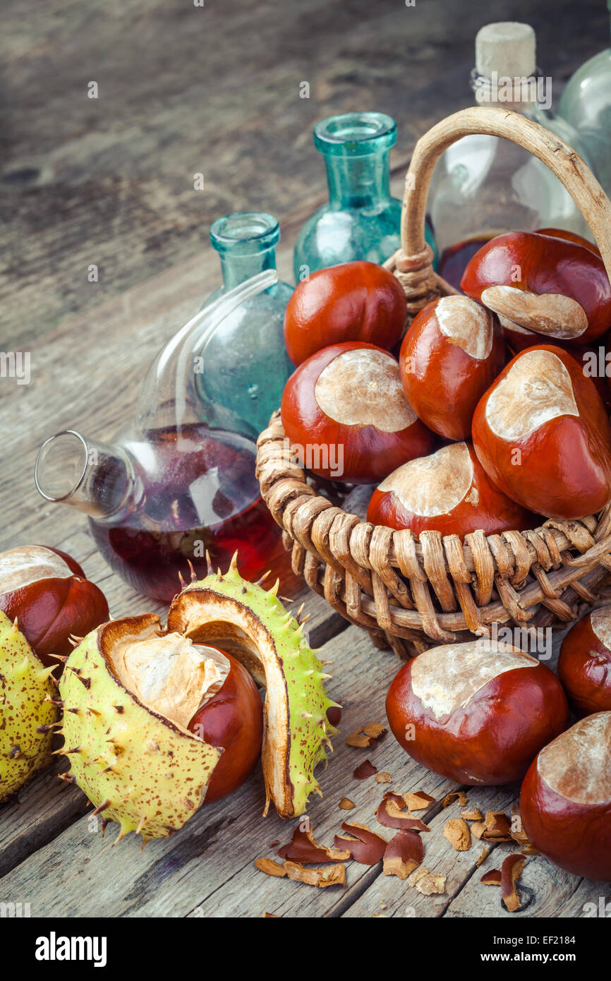 brown chestnuts in basket and vials with tincture on old wooden table Stock Photo