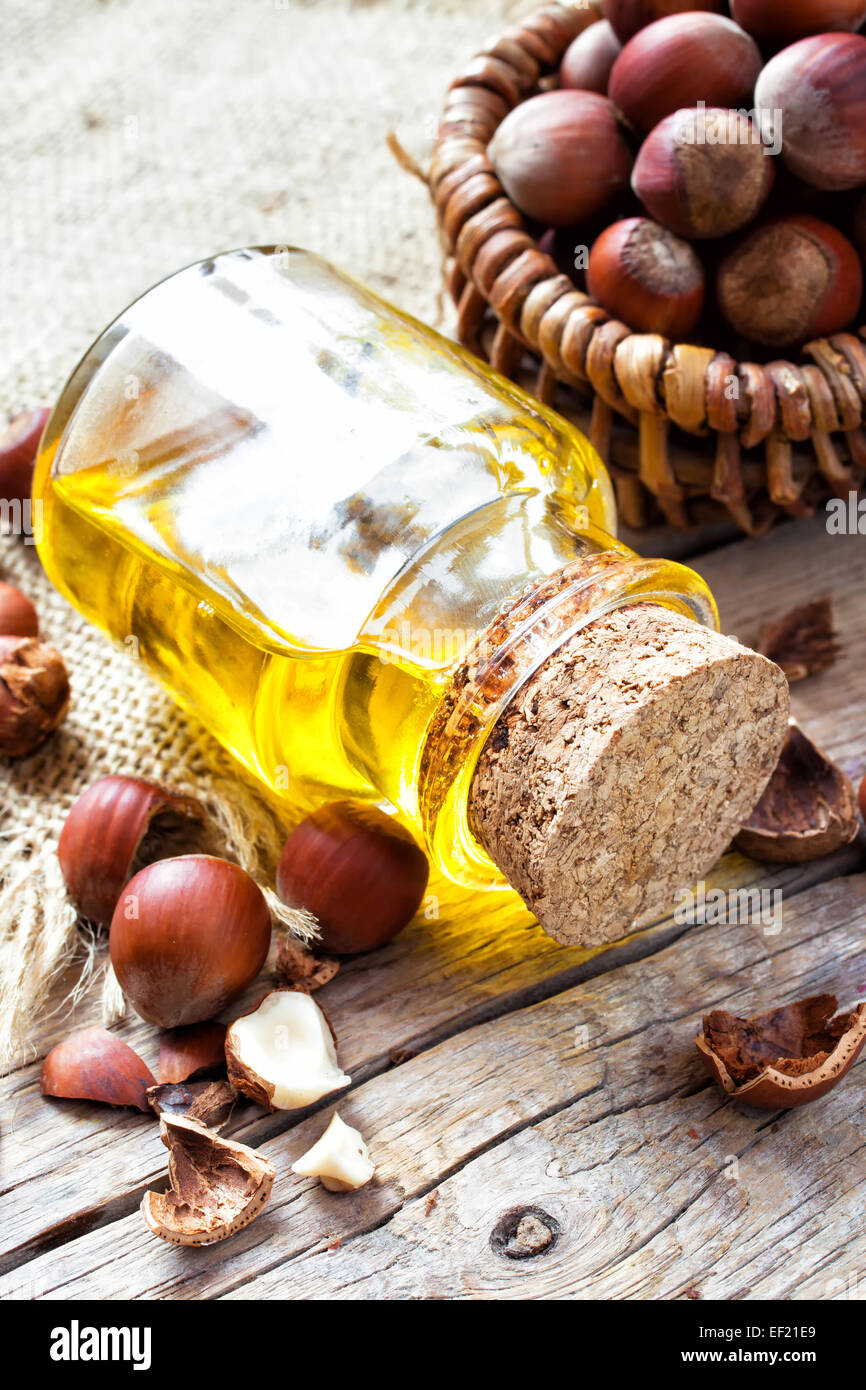 Bottle of healthy nut oil and basket with hazelnuts on old kitchen table. Top view Stock Photo