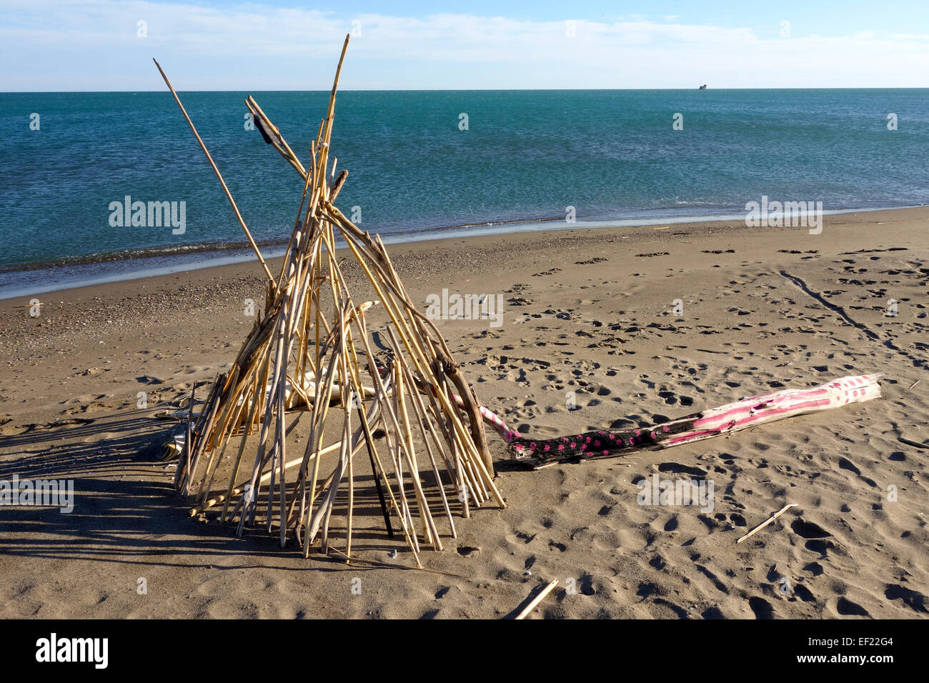 Tipi, tepee, teepee build from river cane and painted log left behind at beach of Malaga, Spain. Stock Photo