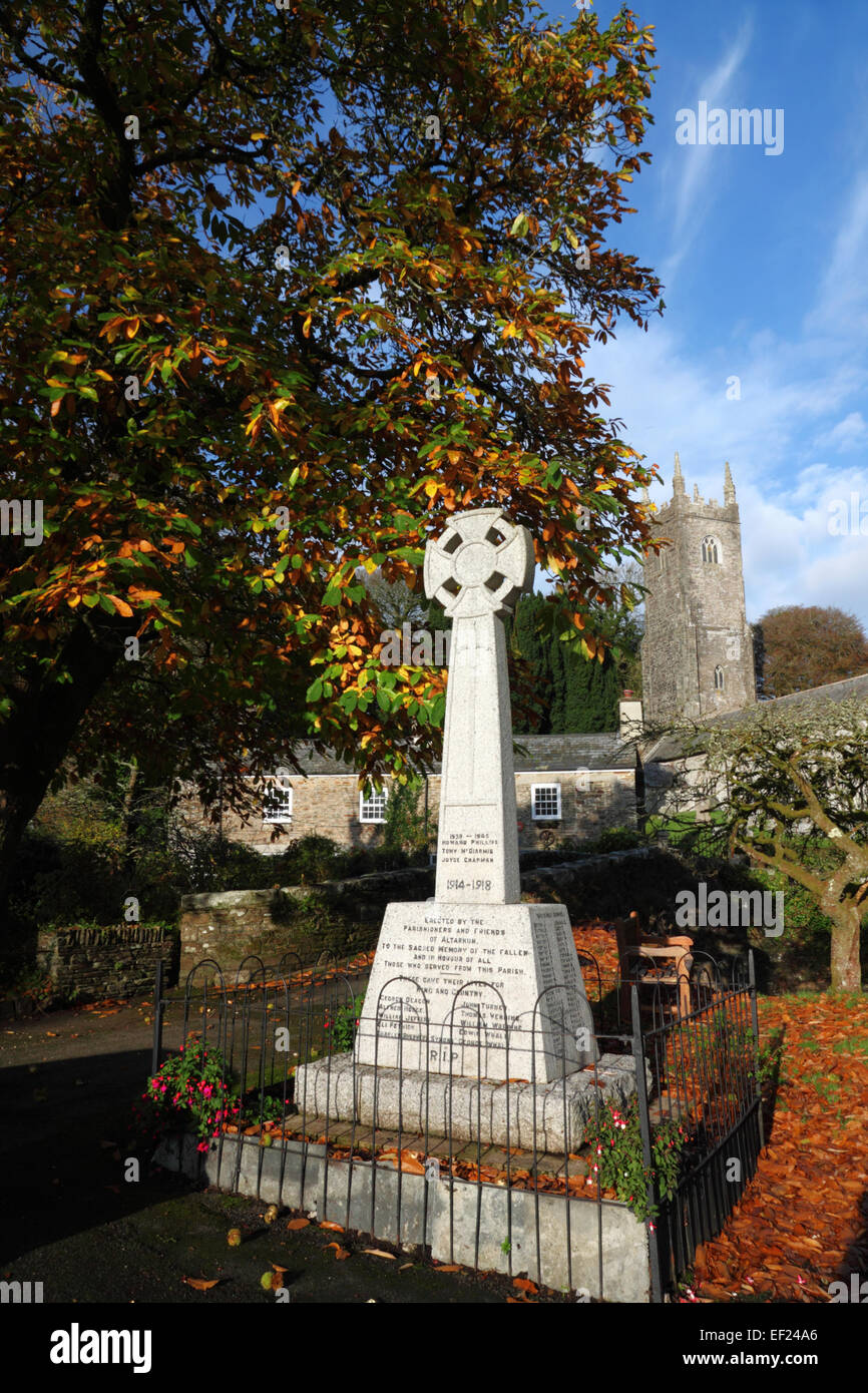 A Celtic Cross war memorial under a tree in autumn foliage and a church tower behind. Stock Photo