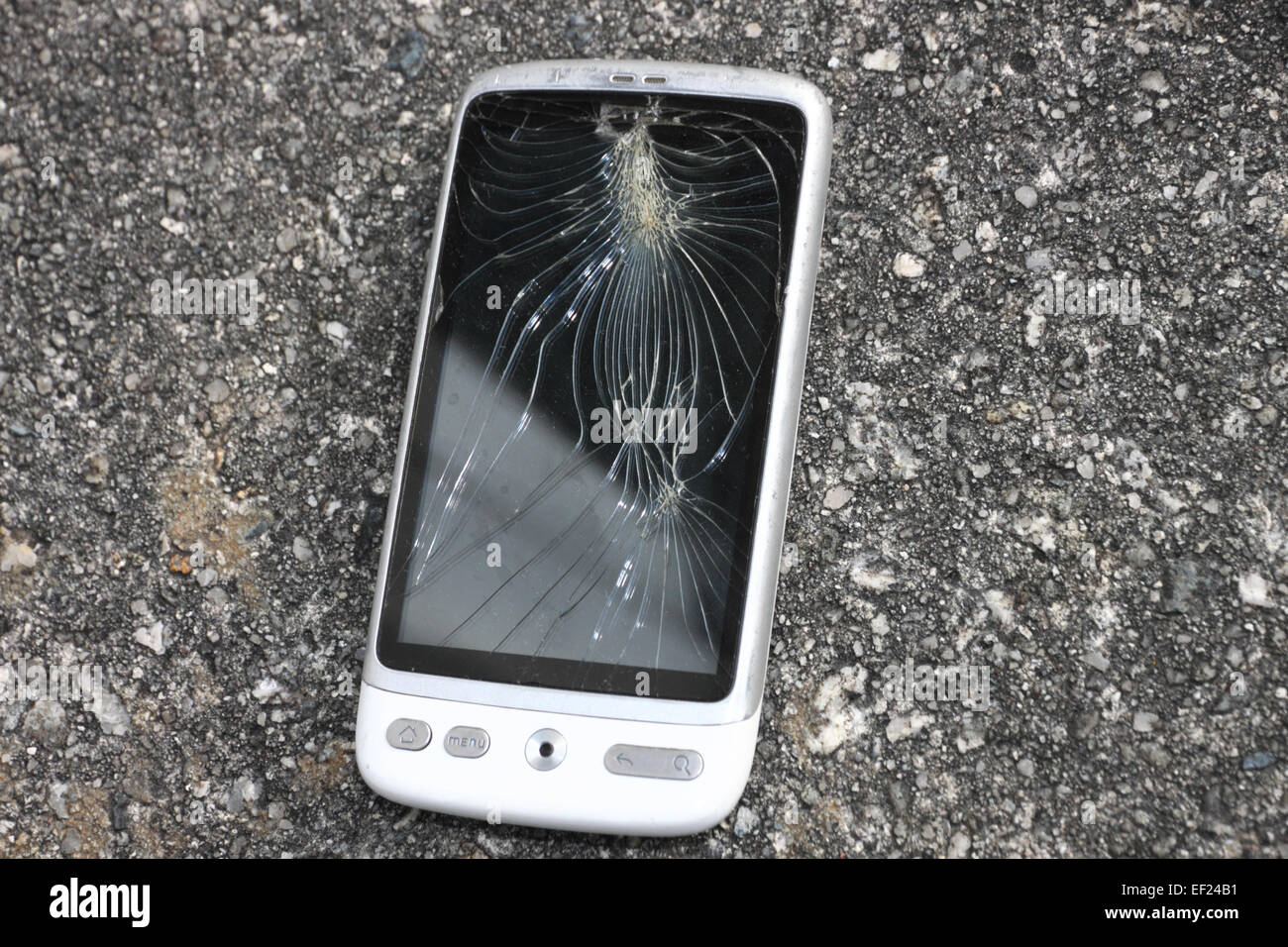 A white HTC 'phone with a smashed touchscreen on concrete. Stock Photo