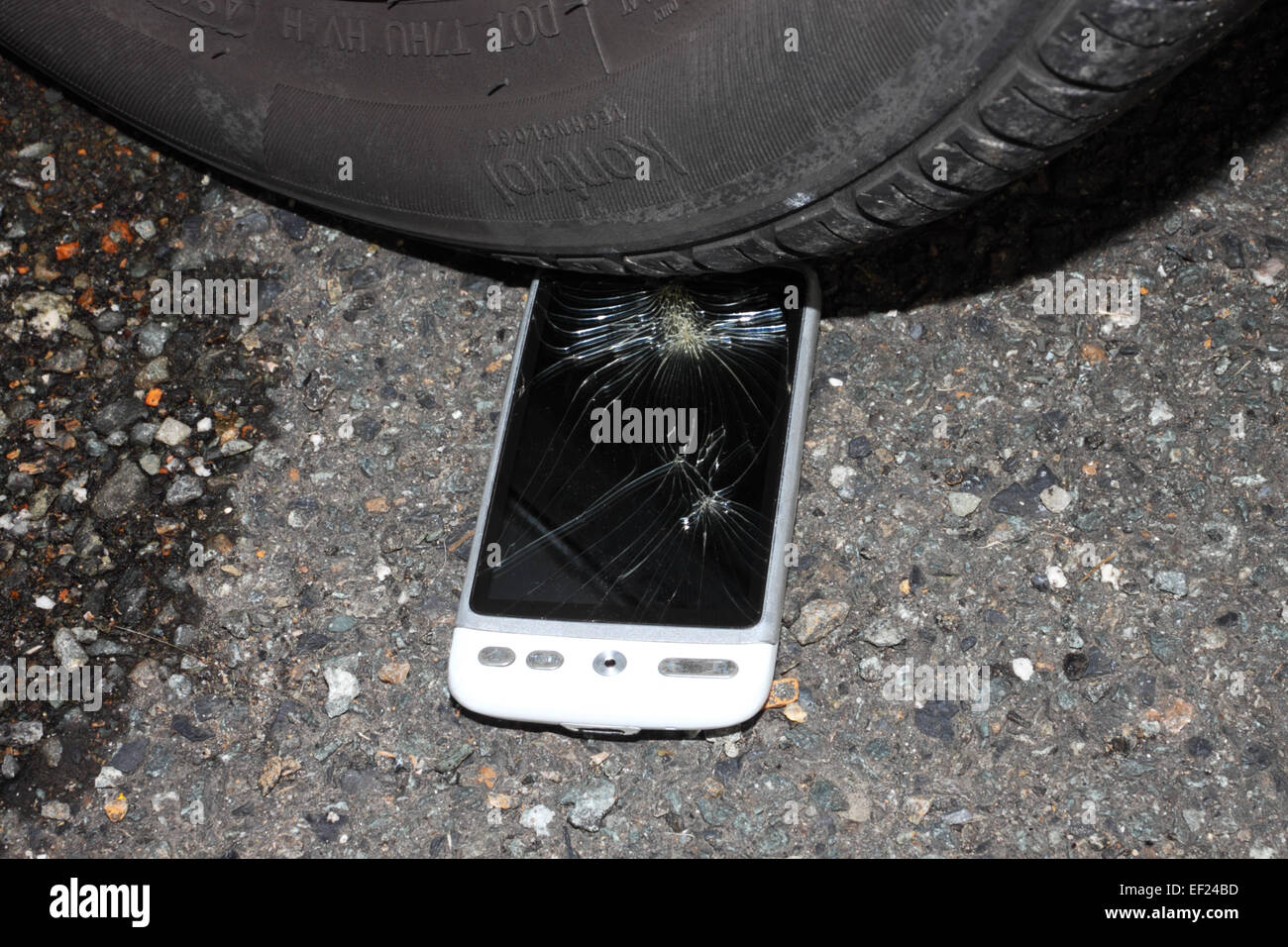 A white HTC 'phone with a smashed touchscreen on a road surface under a