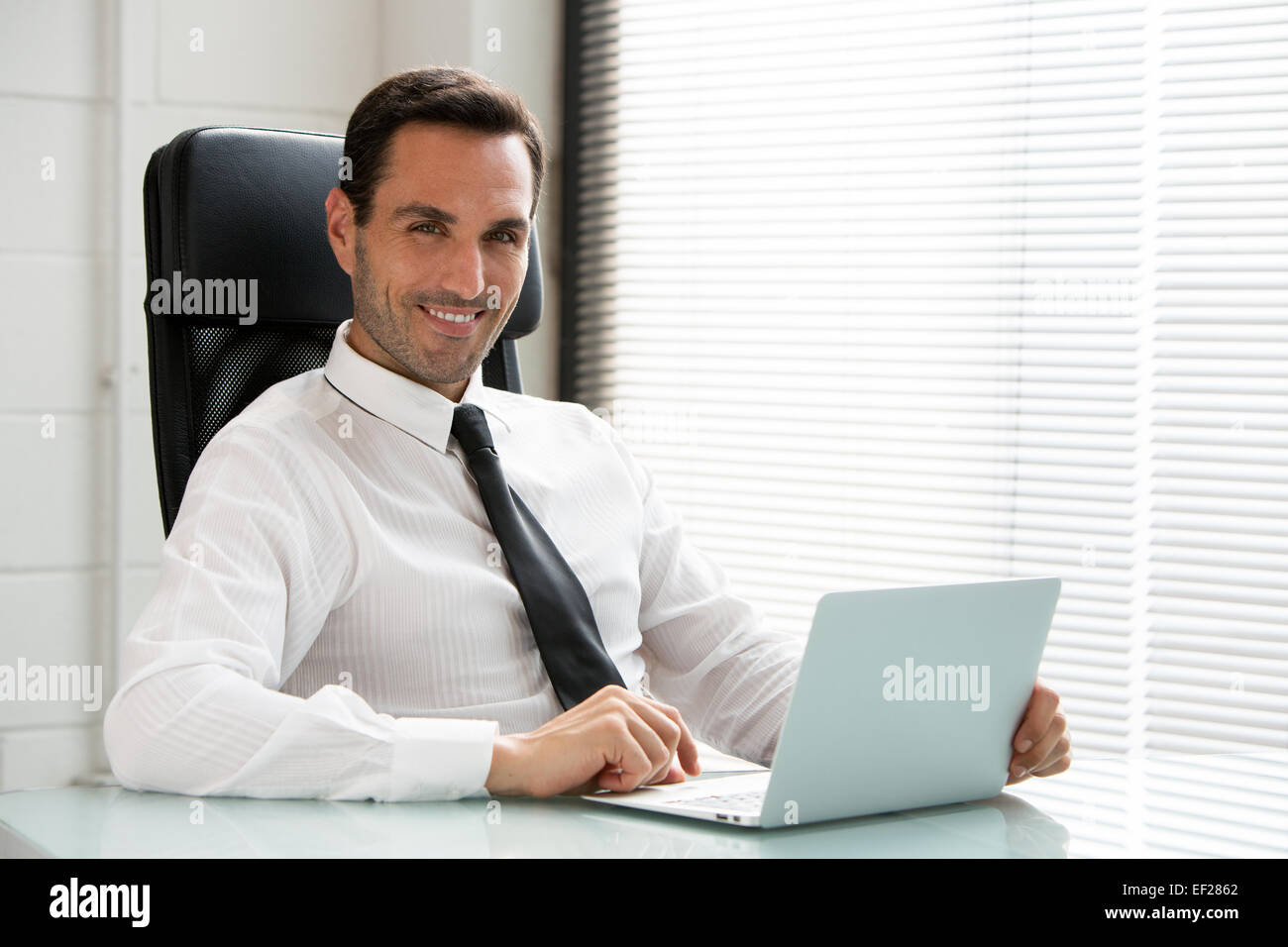 Half length portrait of a male businessman, smiling at camera and working with a laptop computer Stock Photo