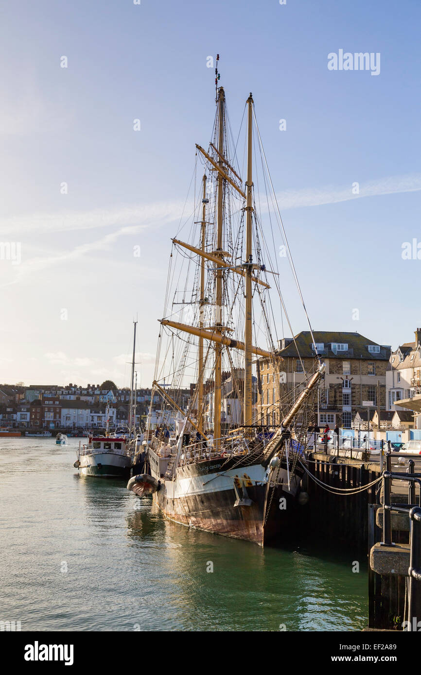 A tall ship is seen in Weymouth harbour moored up at the dock side on a sunny day with blue skies and very light cloud. Stock Photo
