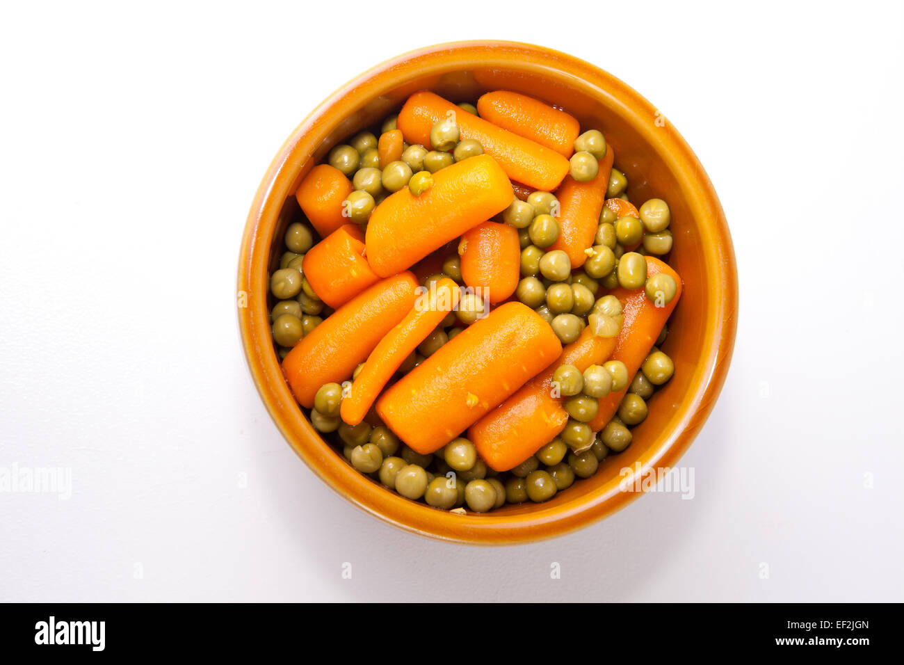 Boiled carrots and green peas on rustic glazed clay bowl. Isolated over