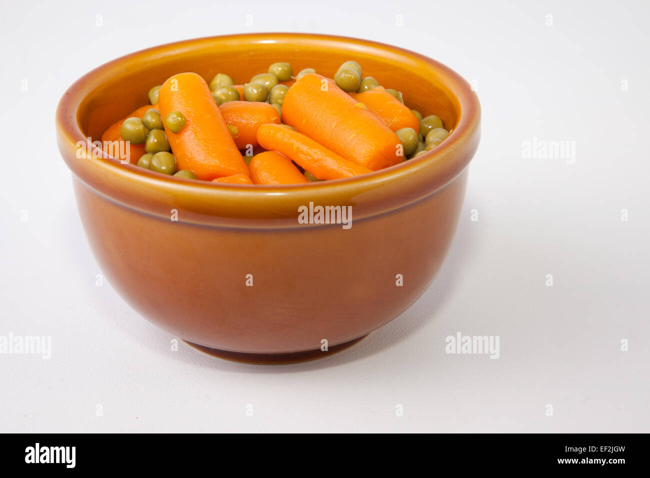 Boiled carrots and green peas on rustic glazed clay bowl. Isolated over