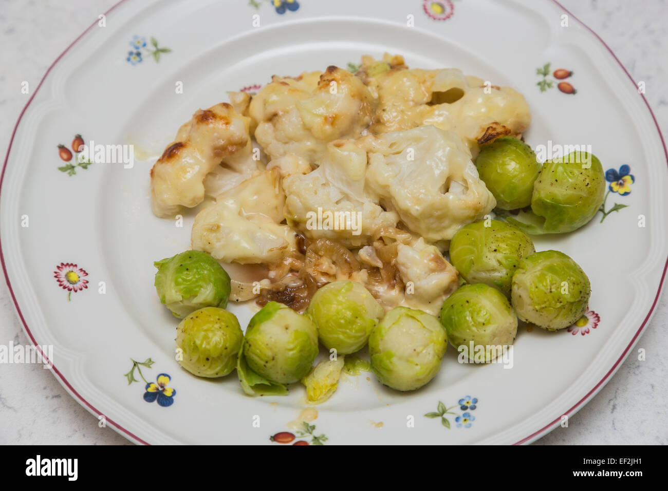 Brassica vegetarian dish: Healthy home cooked cauliflower cheese with Brussels sprouts served on a white china plate with small coloured flowers Stock Photo