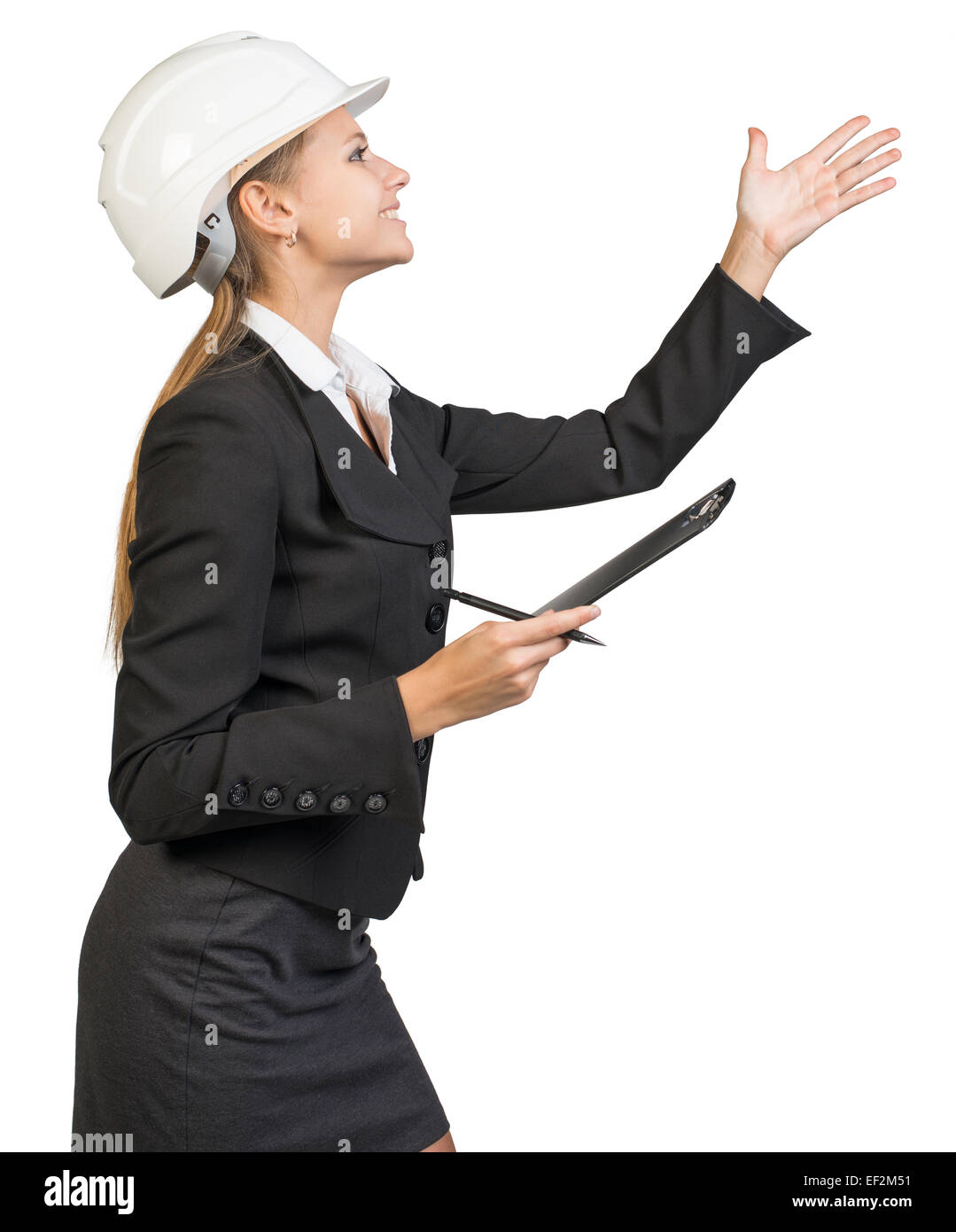 Businesswoman wearing hard hat, with clipboard and pen, pointing Stock