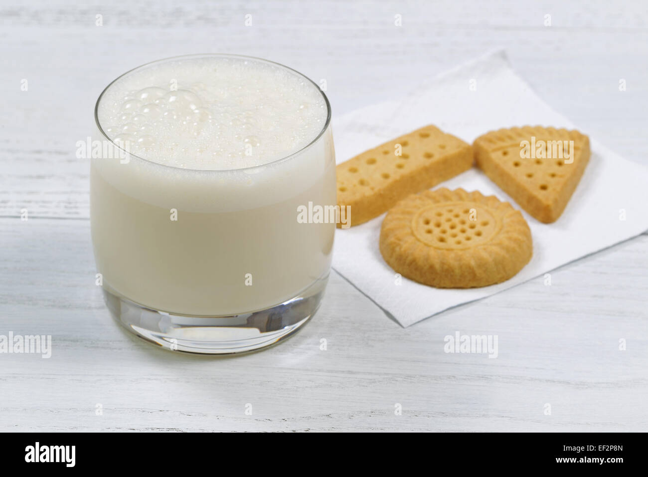 Close up shot of a glass of freshly poured milk with cookies in the background on white wooden table. Stock Photo