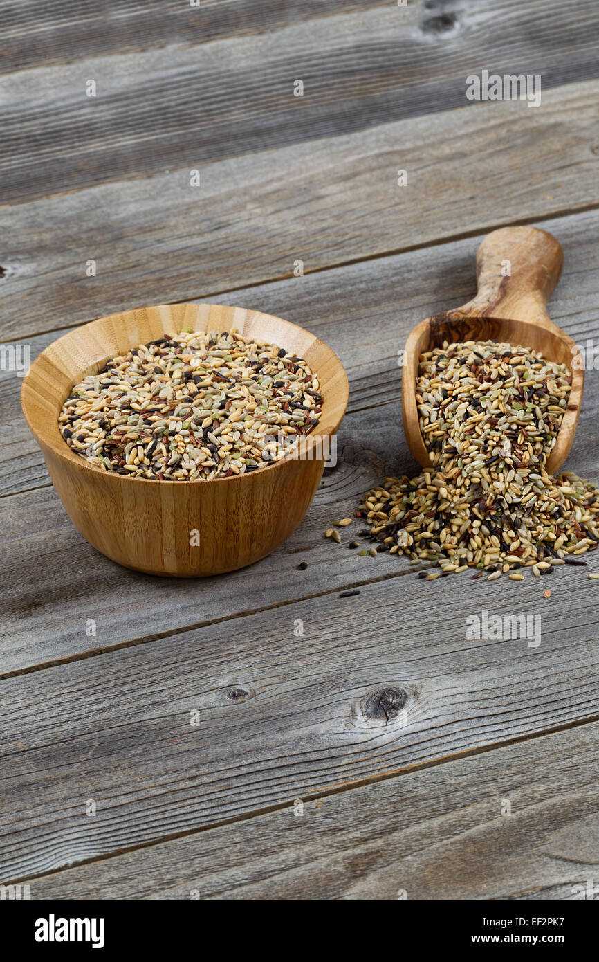 Vertical orientation of a wooden bowl and scoop filled with whole grain rice spilling onto rustic wood Stock Photo