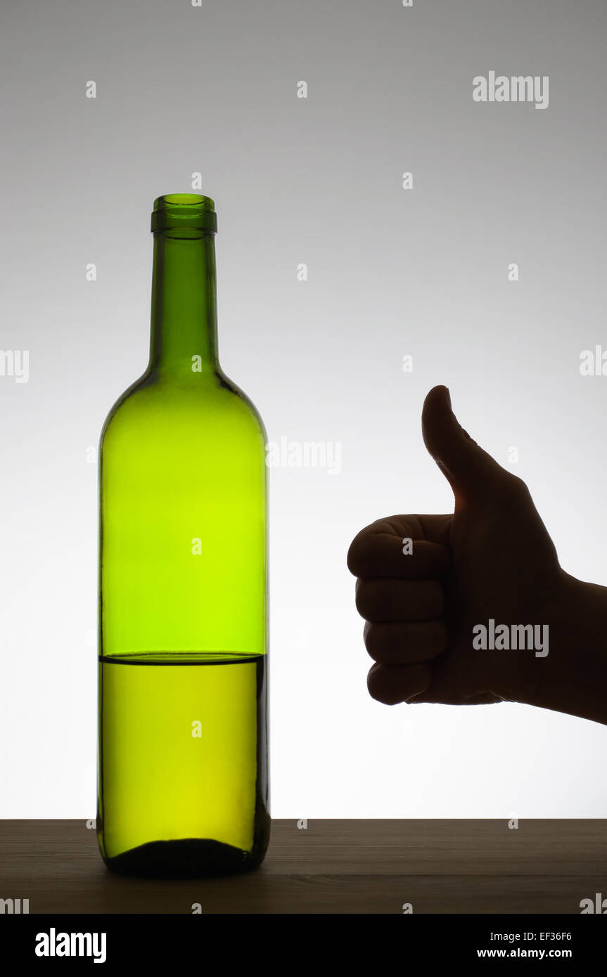 Silhouette of a hand showing thumbs up gesture next to a bottle of wine Stock Photo