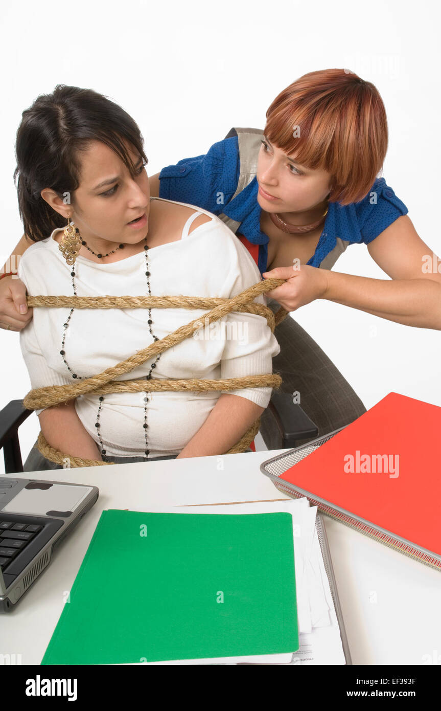 Woman tying rope around woman sitting at desk Stock Photo