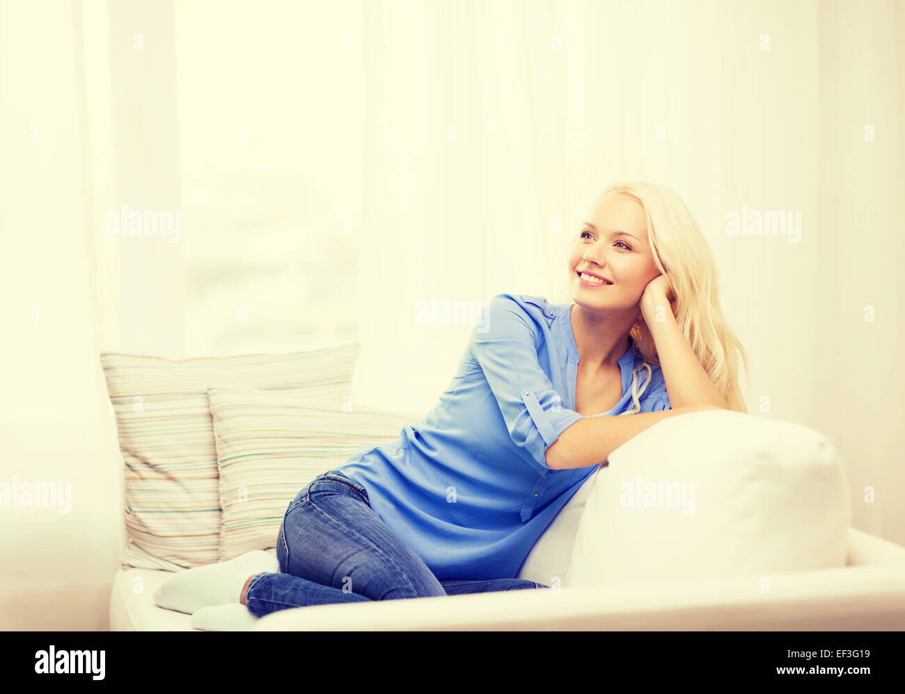 smiling young woman lying on sofa at home Stock Photo - Alamy