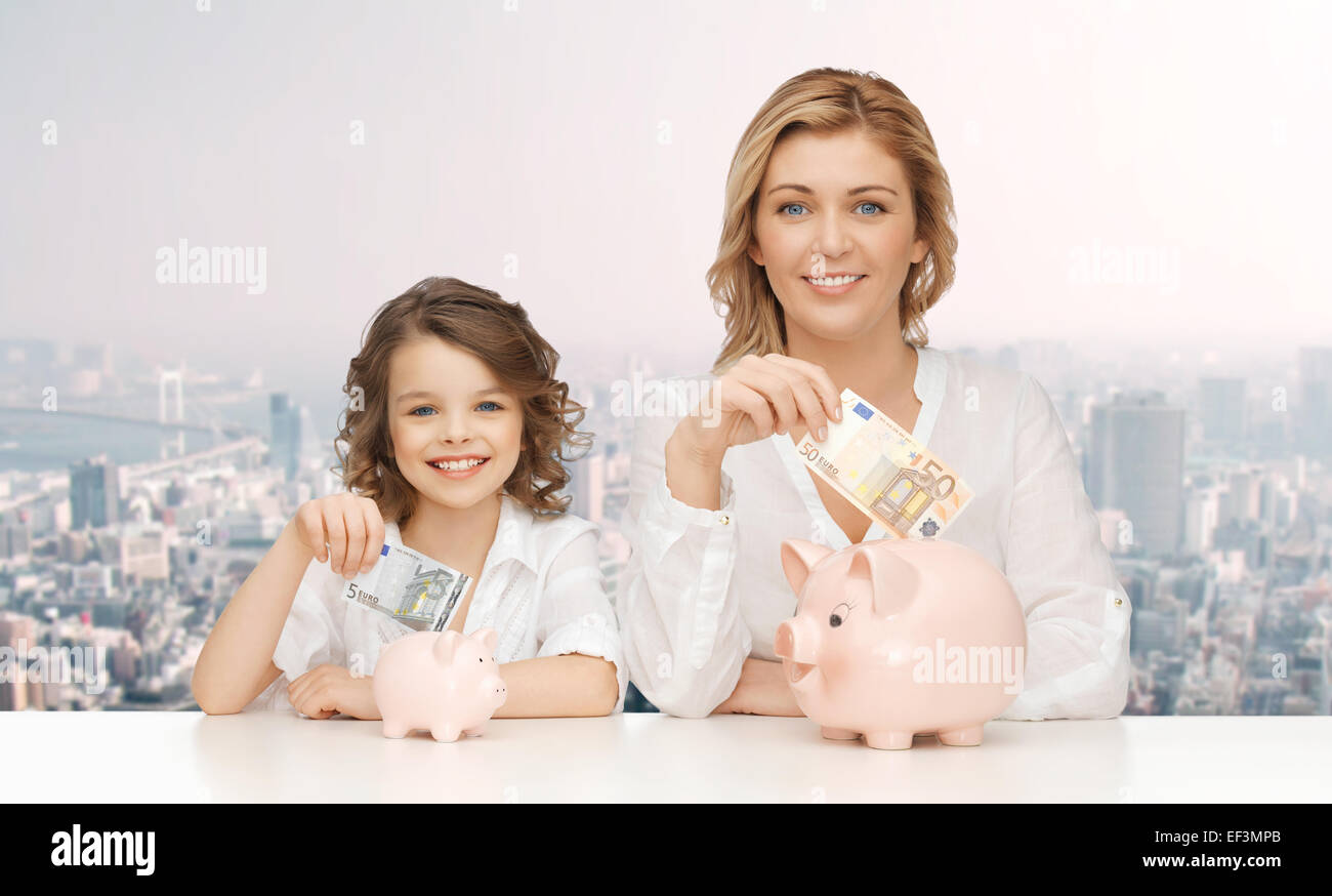 mother and daughter putting money to piggy banks Stock Photo - Alamy