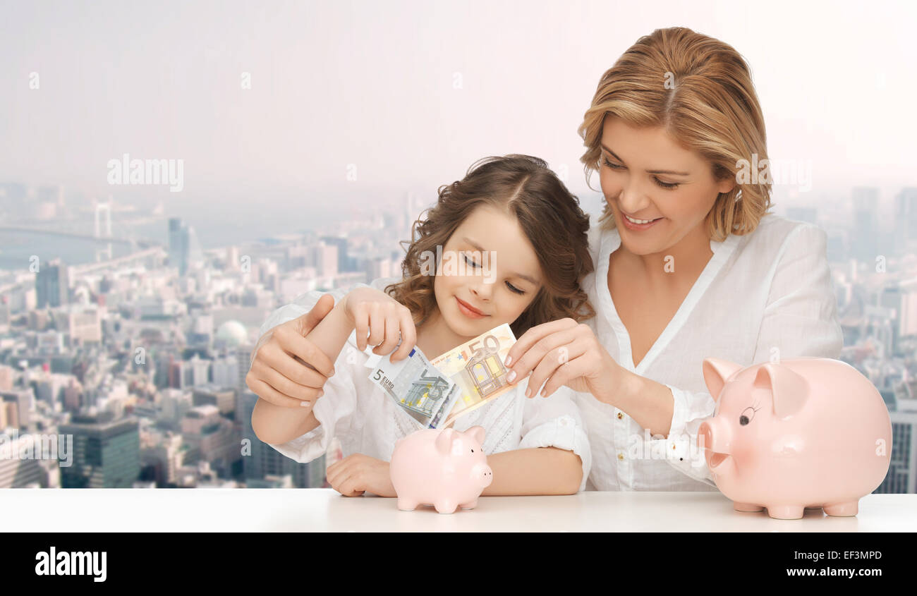 mother and daughter putting money to piggy banks Stock Photo - Alamy