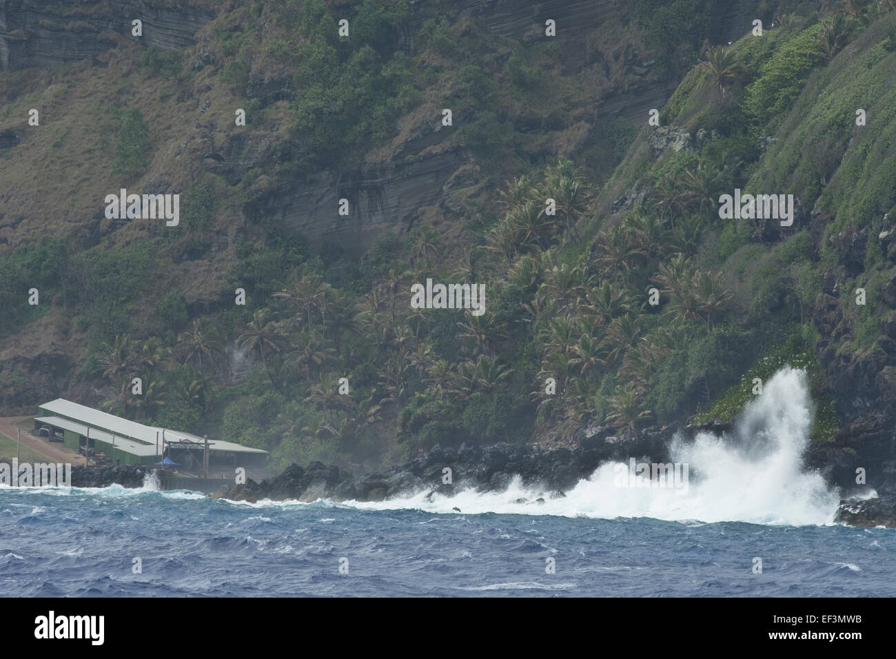 Pitcairn Islands, Pitcairn. Coastal view of rugged volcanic shore. Crashing waves around the boathouse (L) and landing site. Stock Photo