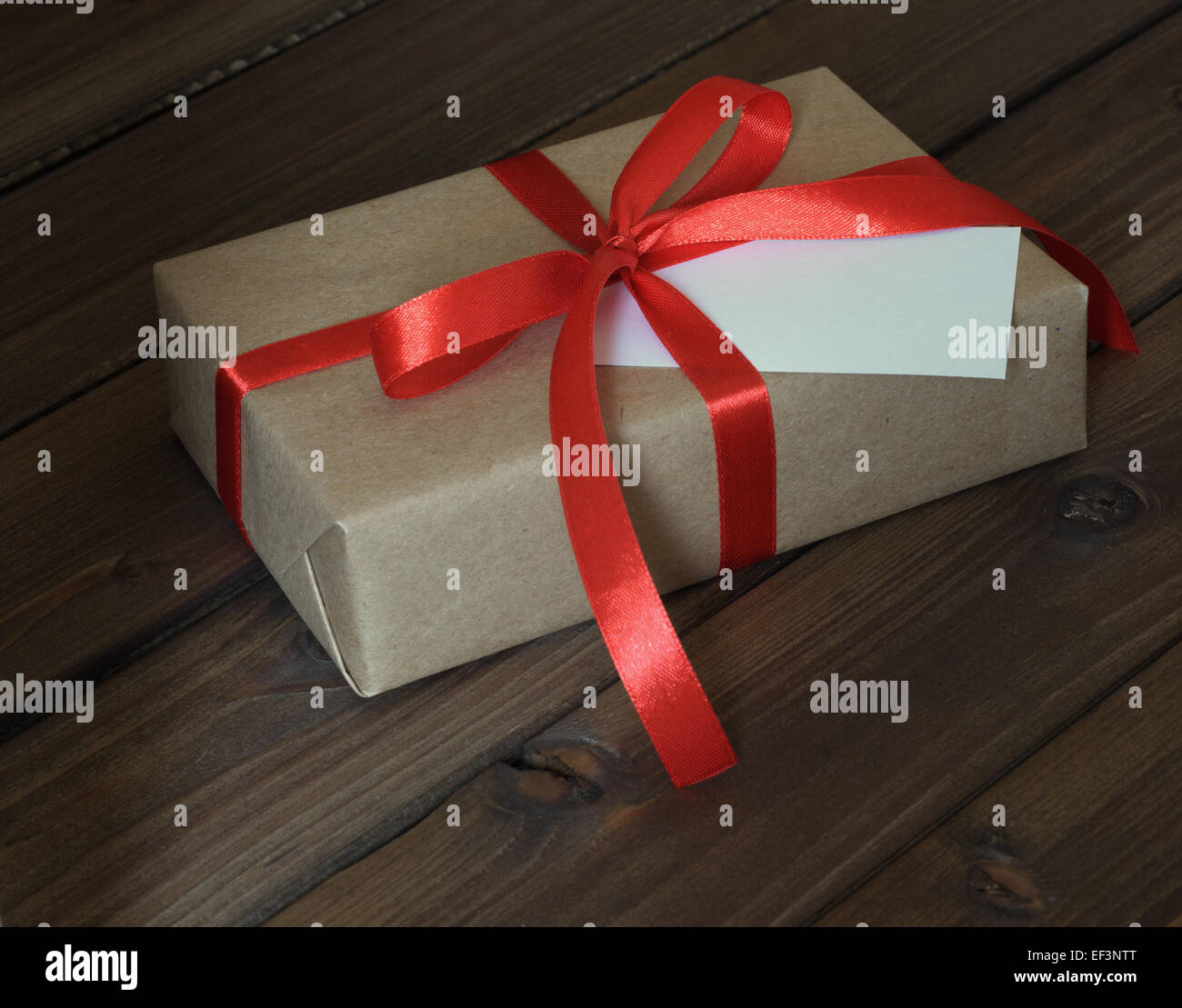 Vintage gift box wrapped in kraft paper and red ribbon on wooden background Stock Photo