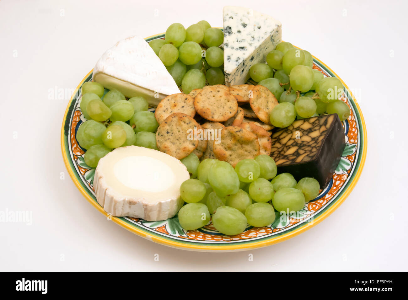 A cheese tray with 4 types of cheese with grapes and crackers on a