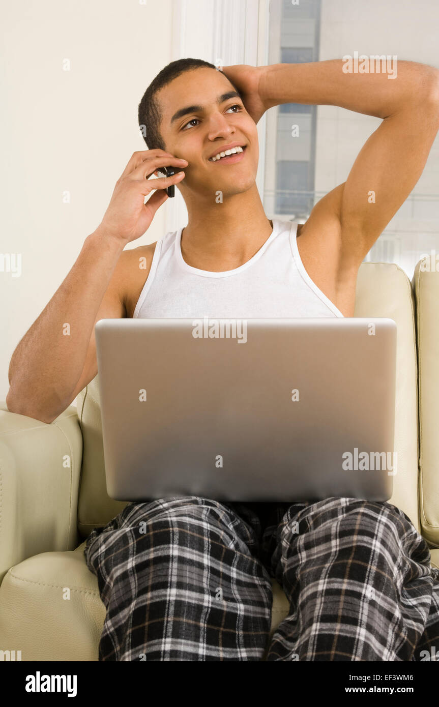 Man talking on phone with laptop on his lap Stock Photo