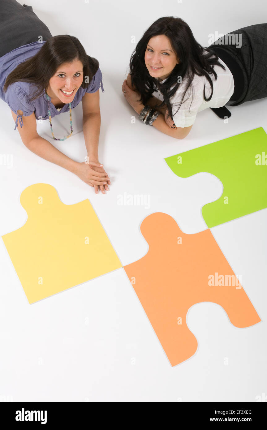 Two women lying on floor beside large puzzle pieces Stock Photo