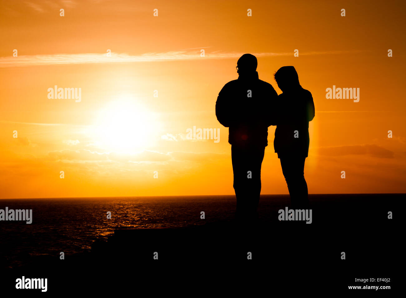 People in silhouette against a setting sun over the sea, Portland Bill, Dorset, UK Stock Photo