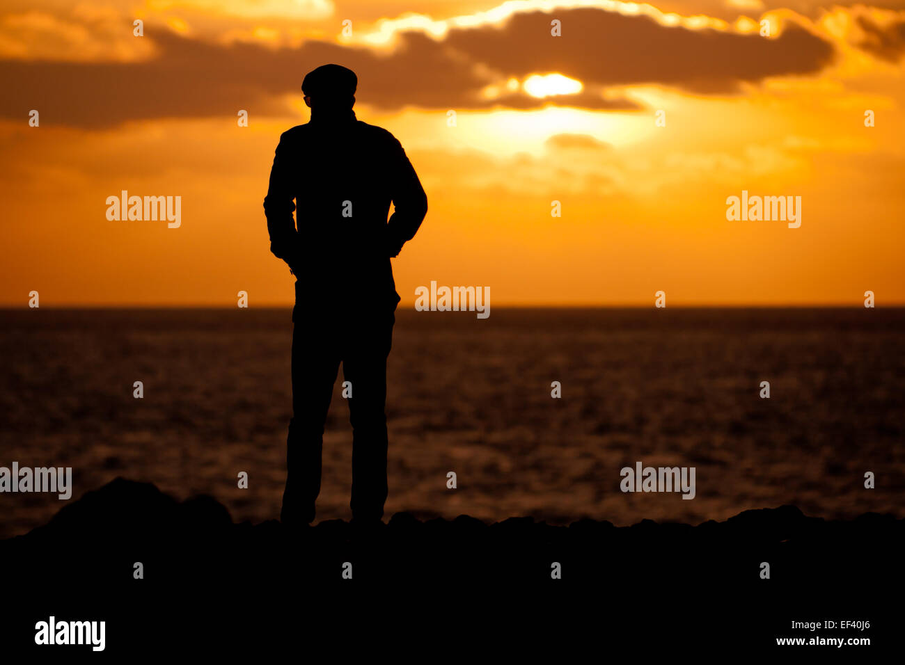 Man in silhouette against a setting sun over the sea, Portland Bill, Dorset, UK Stock Photo