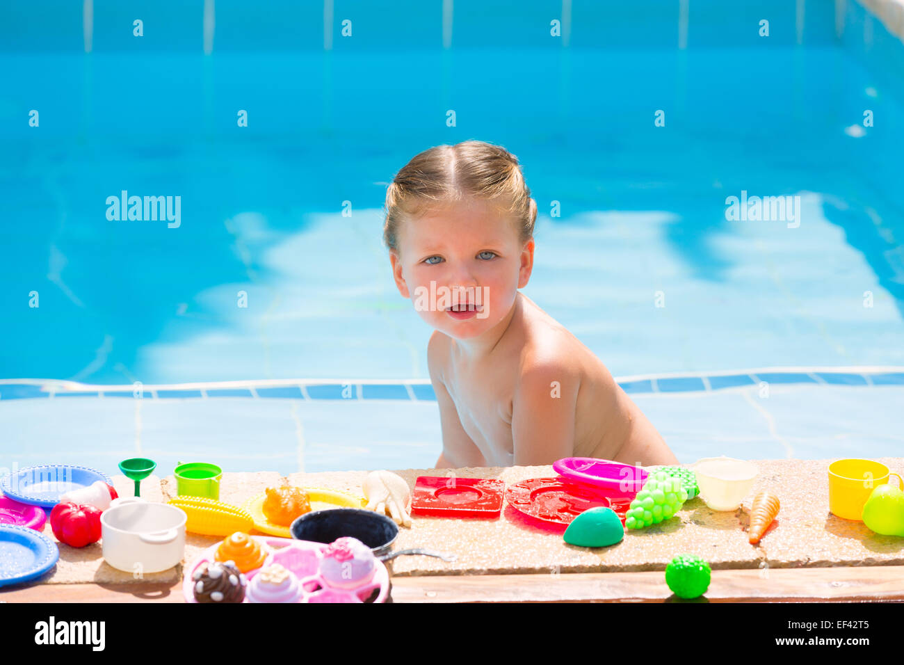 Toddler kid girl playing with food toys in swimming pool at summer