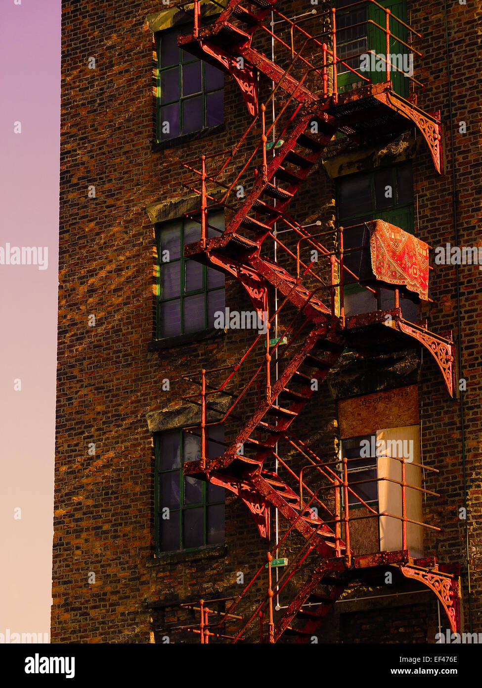 Iron red painted fire escape on a former Manchester cotton mill illuminated in the setting sun. Stock Photo