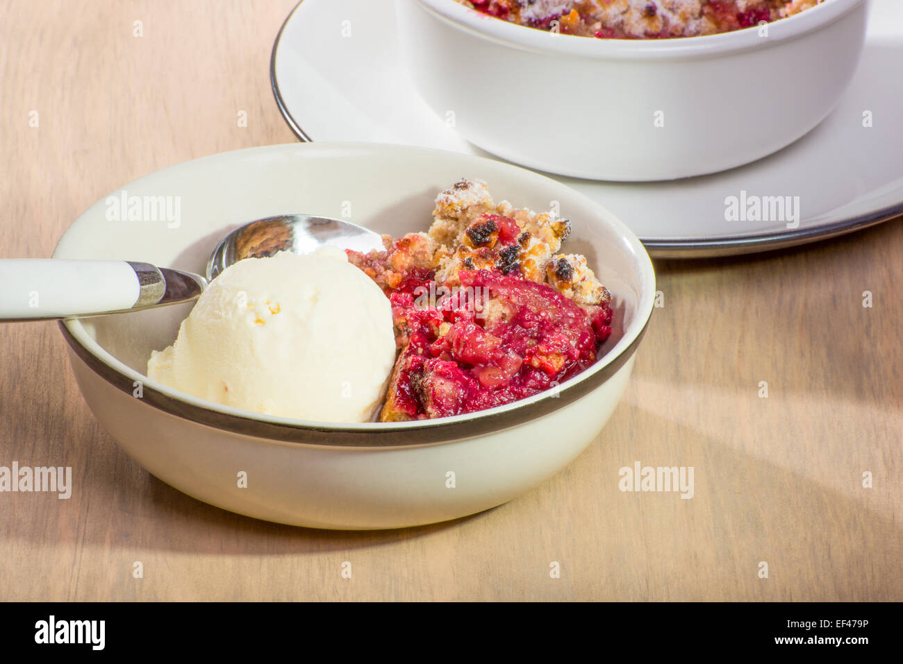 Freshly baked mixed berry crumble in a small dish, served with vanilla ice cream. Stock Photo