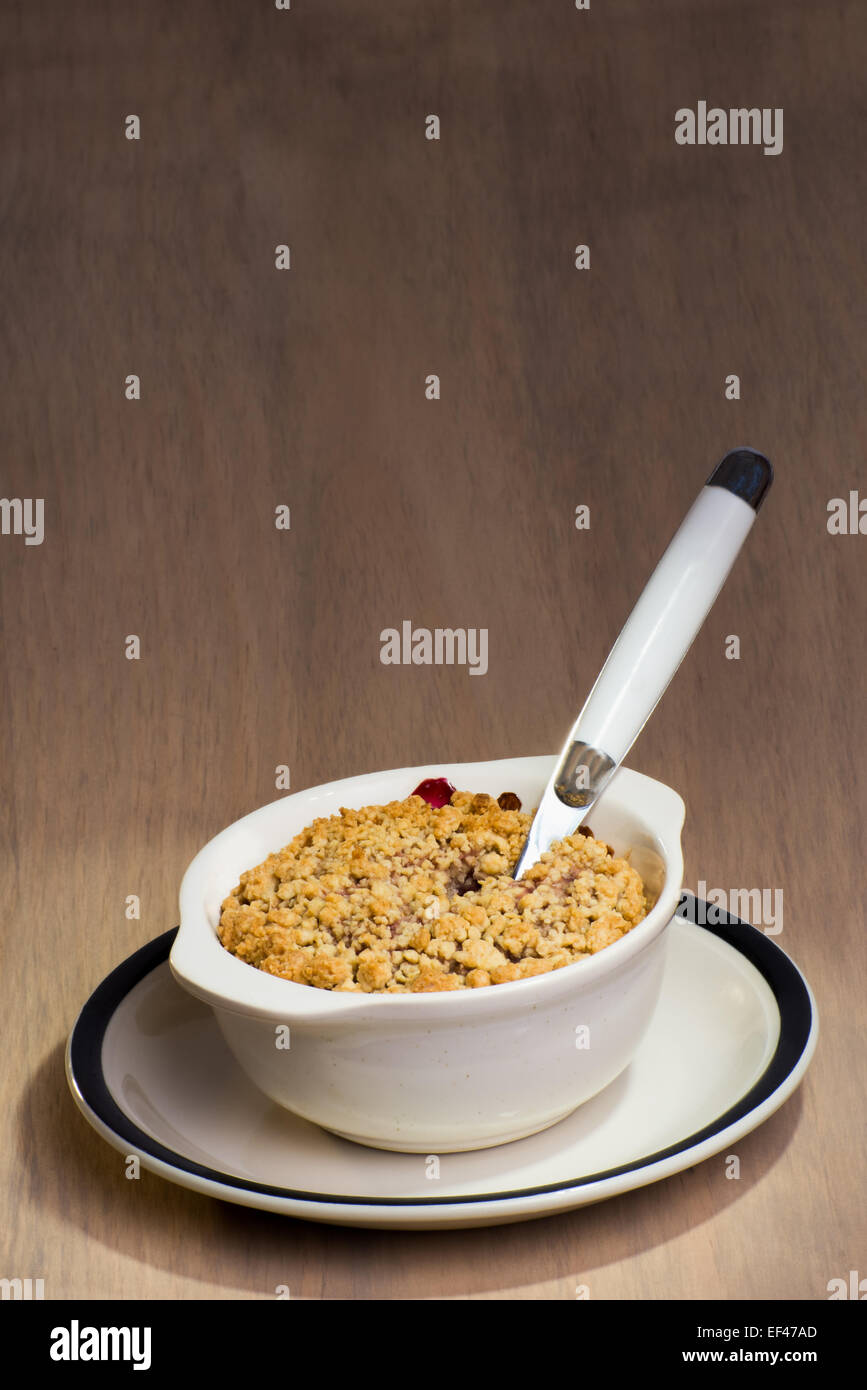 A ceramic dish with freshly baked mixed berry crumble, and a spoon stuck in to the berry crumble. Stock Photo