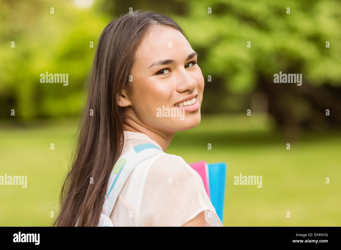 Portrait of a smiling student with a shoulder bag and holding book ...