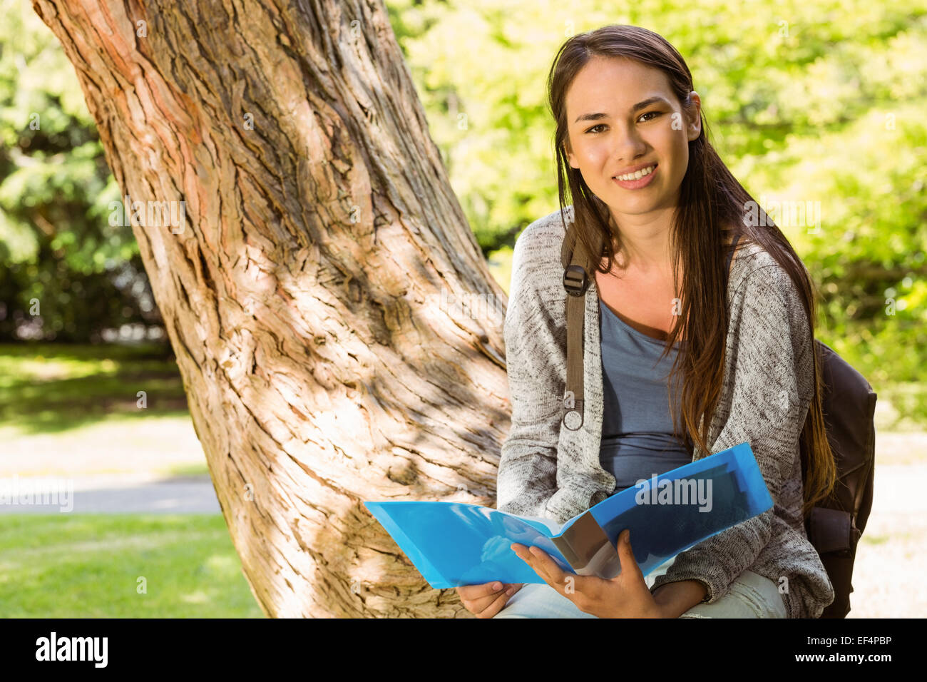 Smiling student sitting on trunk and holding book Stock Photo - Alamy