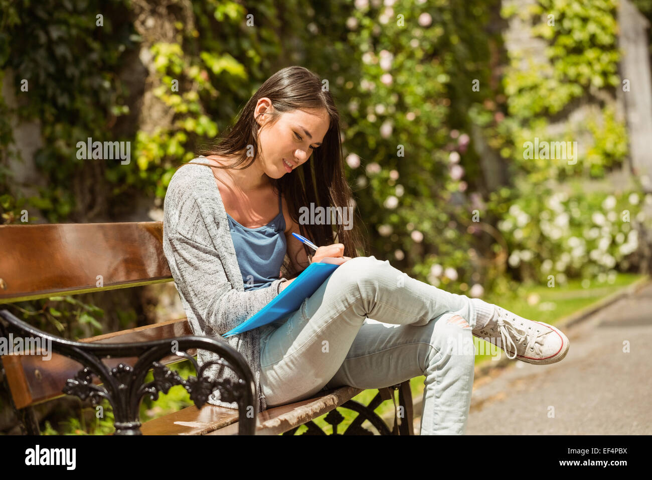 Smiling student sitting on bench and writing on notepad Stock Photo - Alamy