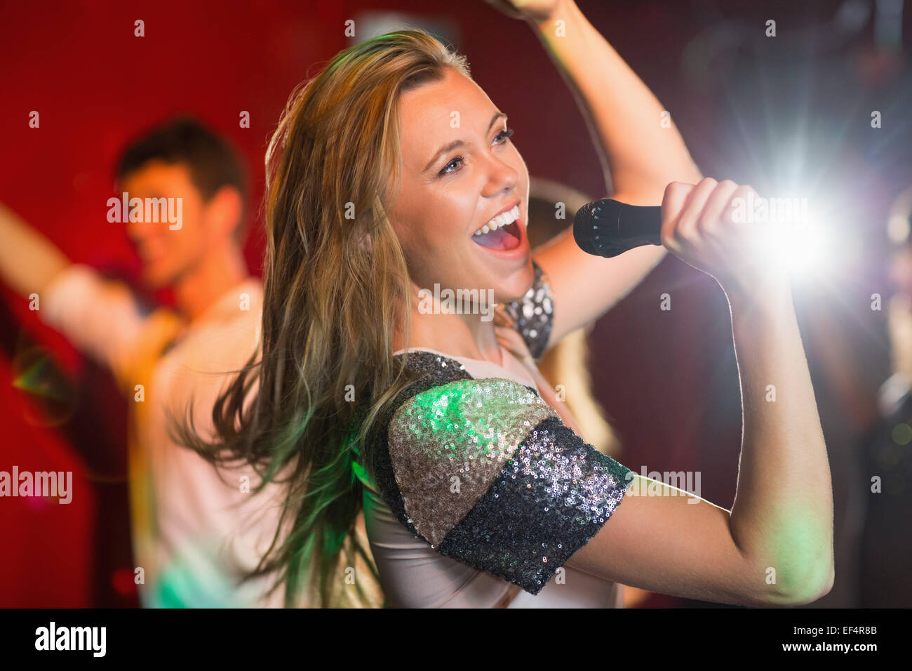Happy blonde singing karaoke into mic Stock Photo