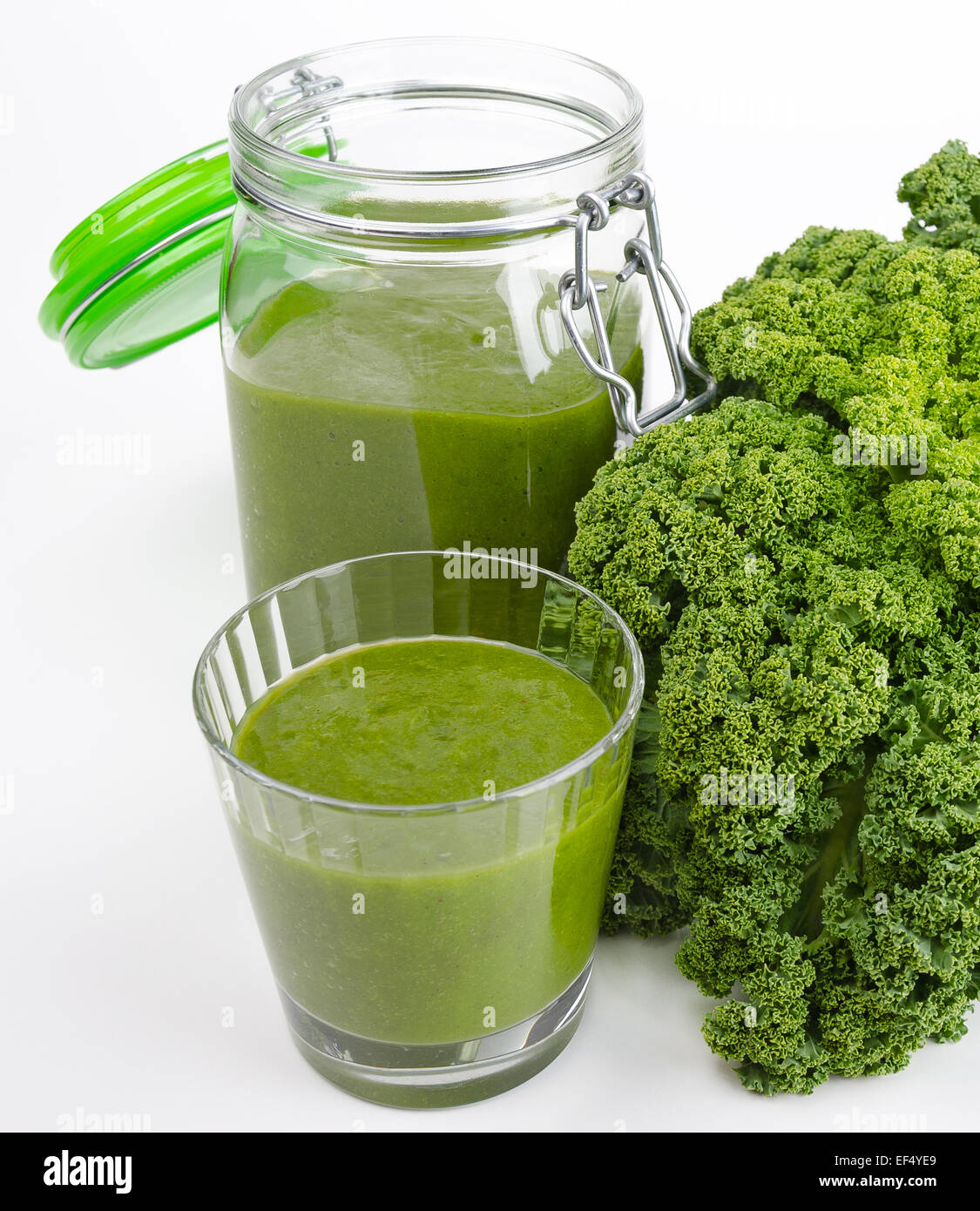 Green smoothie in a glass and in a open jar with fresh kale. A raw, healthy and vegan beverage made of green leafs and fruits. Stock Photo