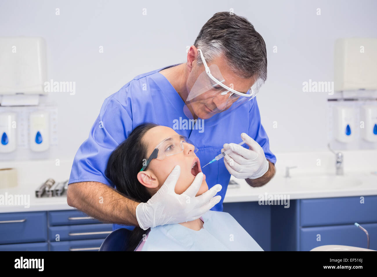 Dentist wearing face shield and doing injection to his patient Stock