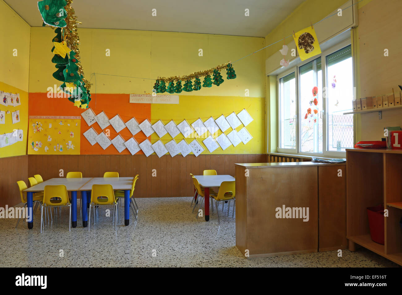 Preschool classroom with yellow chairs and table with drawings of children hanging on the walls Stock Photo