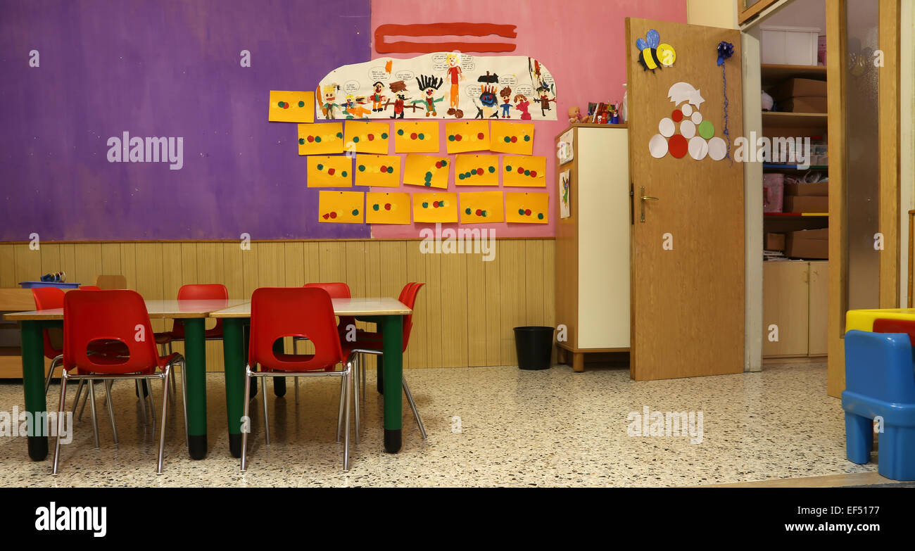 Preschool classroom with red chairs and table with drawings of children hanging on the walls Stock Photo