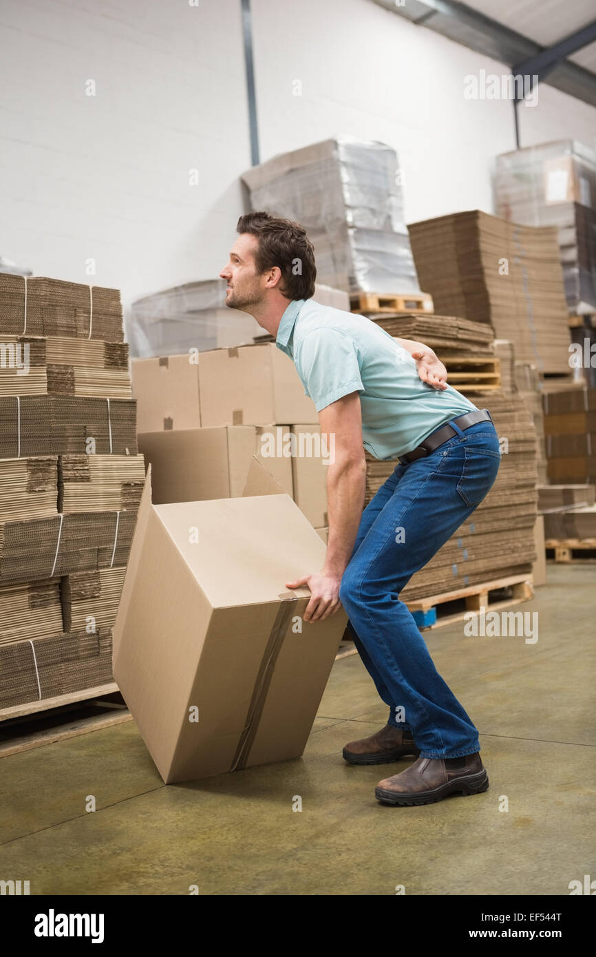 Worker with backache while lifting box in warehouse Stock Photo