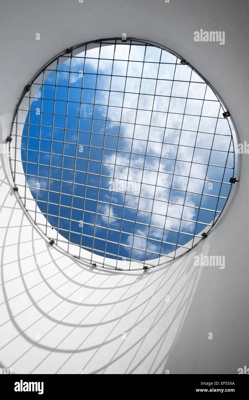 Abstract empty white interior fragment. Blue cloudy sky behind the round window with metal grid Stock Photo
