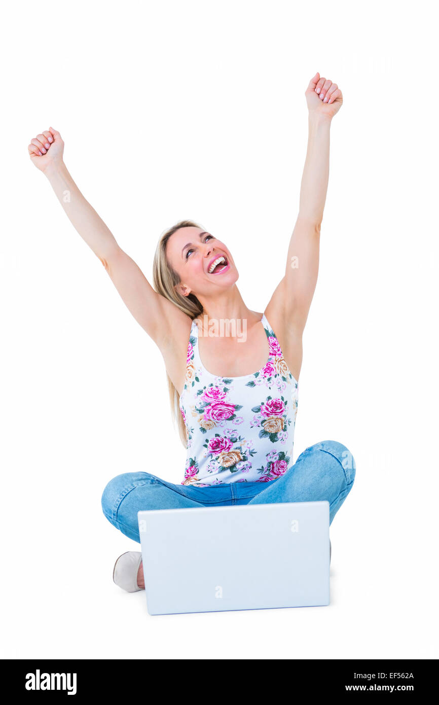 Happy blonde cheering with arms up near her laptop Stock Photo