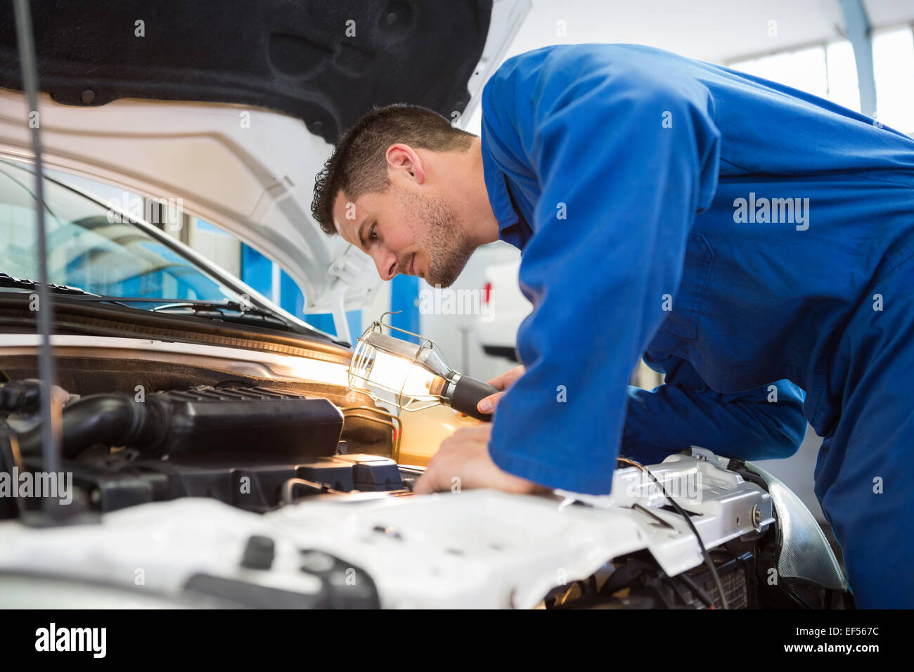 Mechanic examining under hood of car with torch Stock Photo