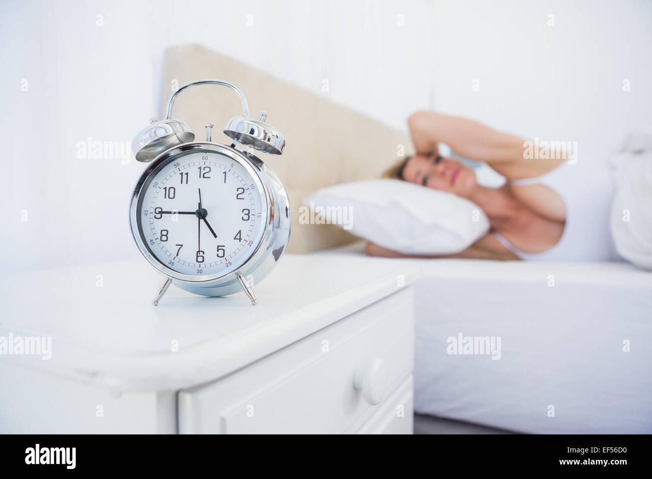 Annoyed woman covering her ears from alarm clock noise in bed Stock