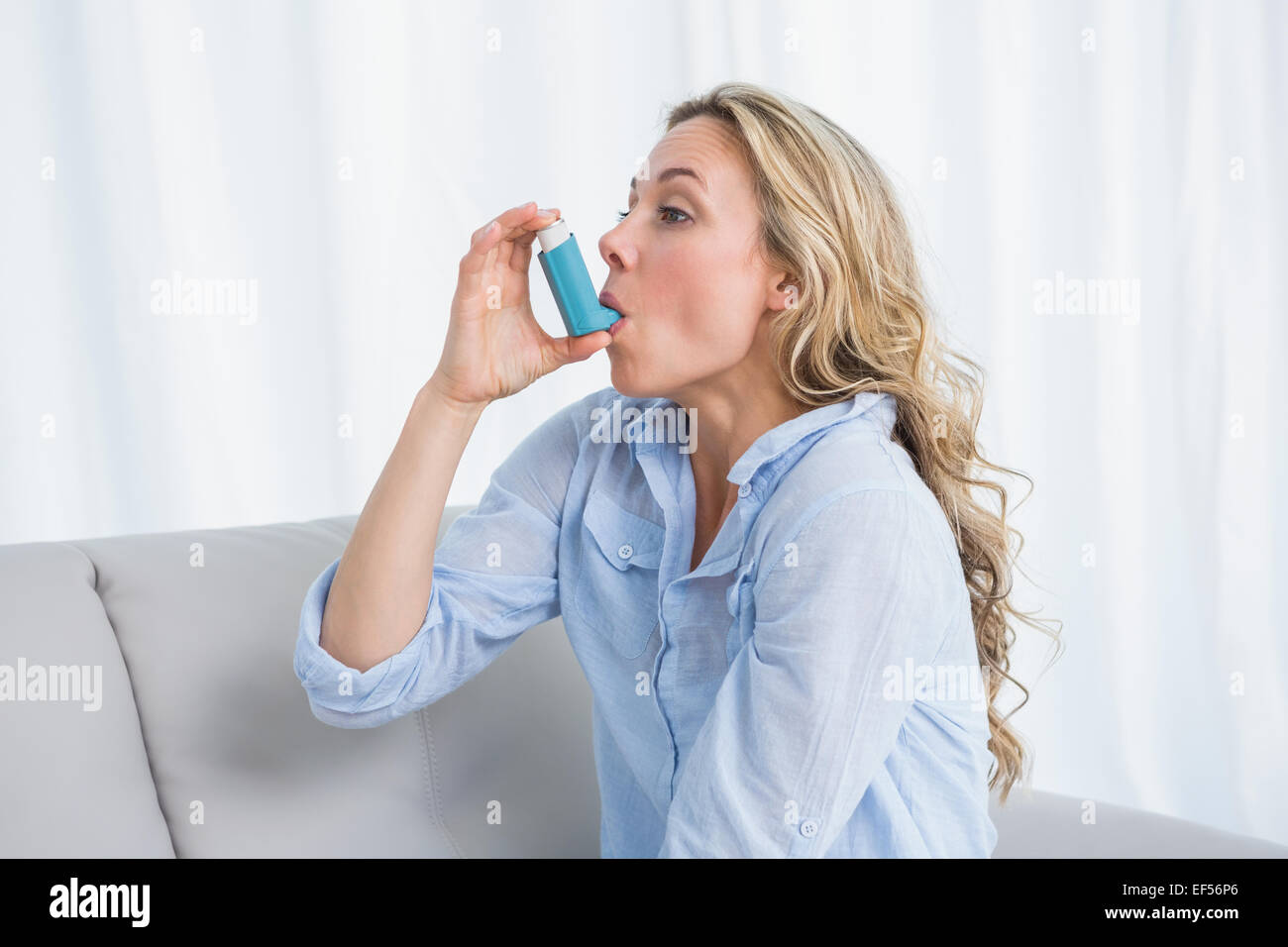 Blonde using her asthma inhaler on couch Stock Photo Alamy