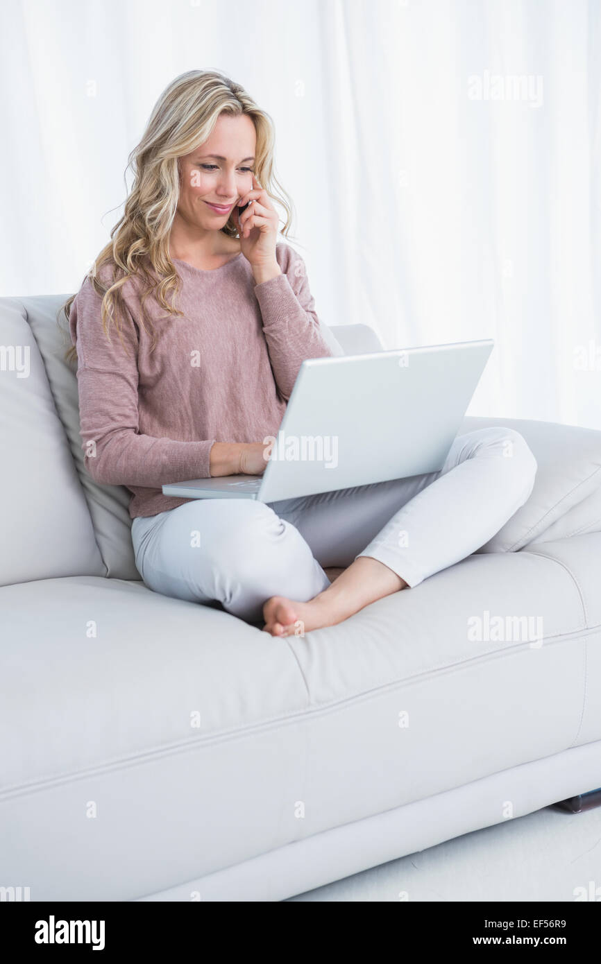 Smiling blonde sitting on couch using laptop Stock Photo - Alamy