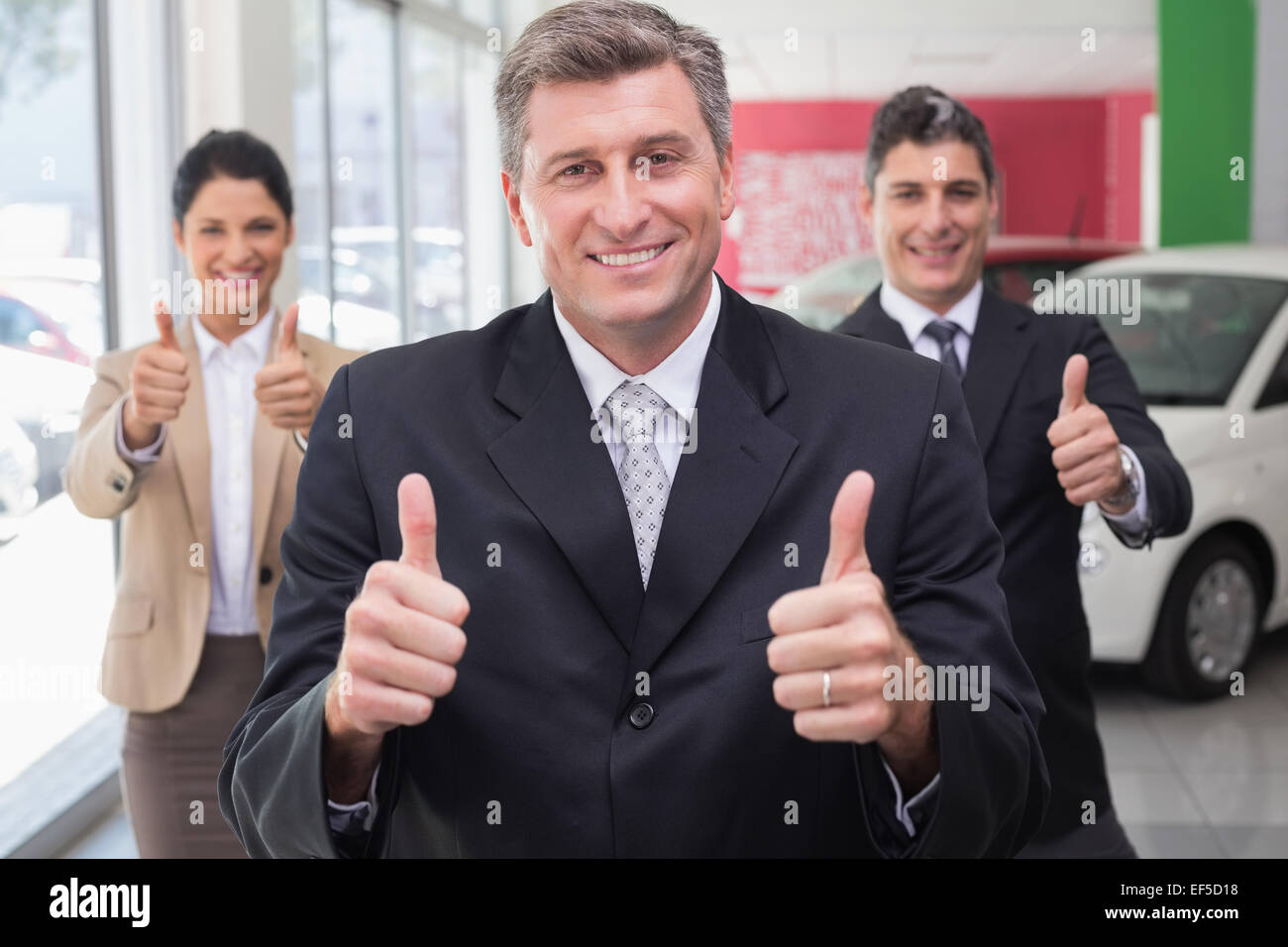 Smiling business team standing while giving thumbs up Stock Photo - Alamy