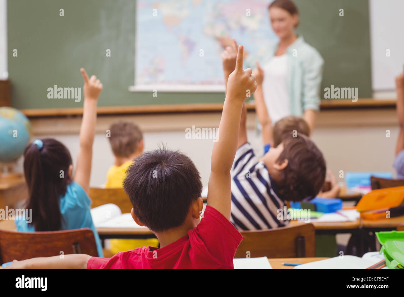 Pupils raising hand during geography lesson in classroom Stock Photo ...