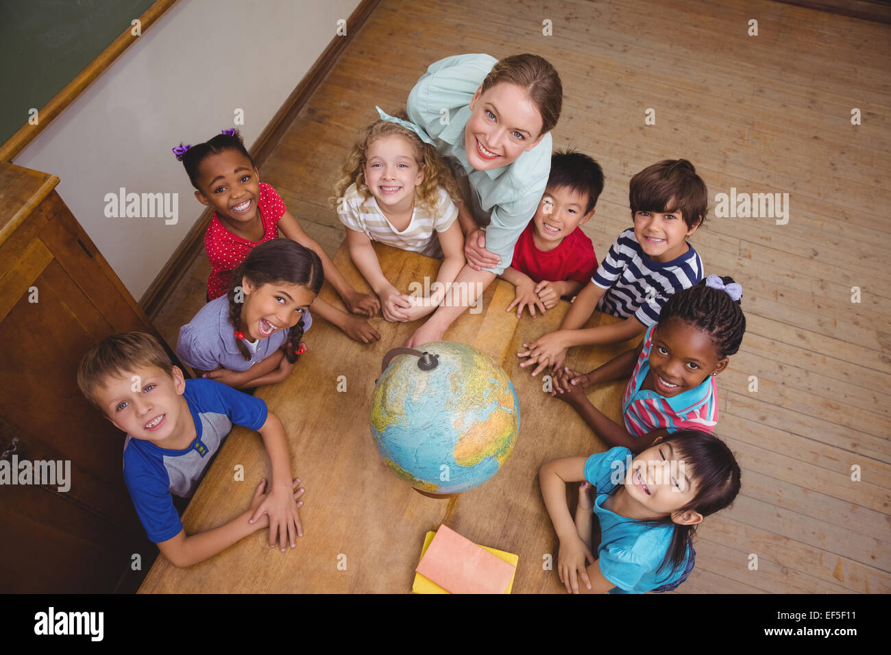 Cute pupils smiling around a globe in classroom with teacher Stock ...